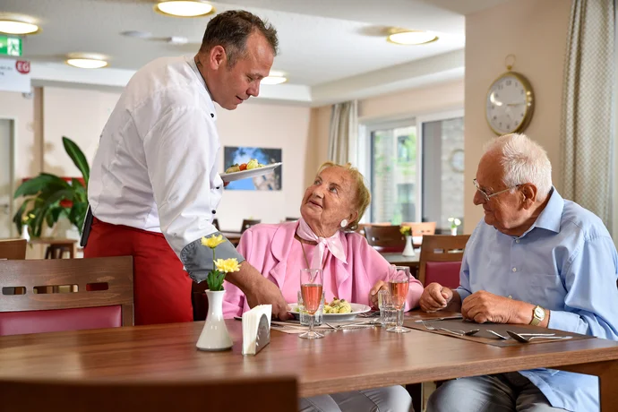 Älteres Ehepaar sitzt im Essensraum in einer Einrichtung der K&S Gruppe und bekommt ihr Menü serviert