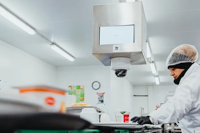 Mitarbeiterin bestückt Tabletts in der Zentralküche am Fließband